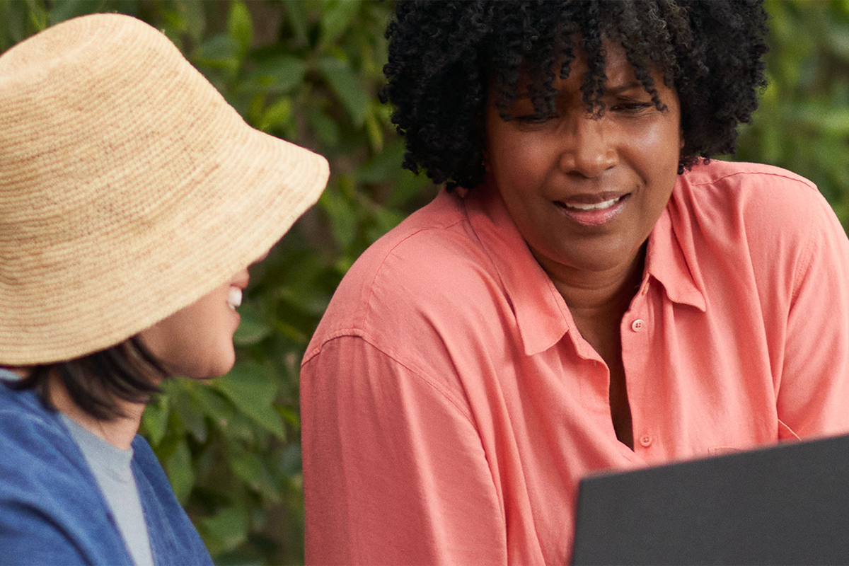 Two women are talking while using a PCSpecialist laptop with Windows 11